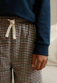 Tumesinise pika varrukaga särk, mida on kombineeritud pruunide ja siniste ruuduliste pidžaamapükstega, millel on valge pael. Särgil on soonikud mansettidel.