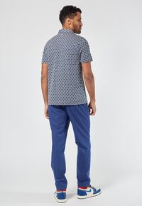 Camicetta a maniche corte con un motivo geometrico blu navy, abbinata a pantaloni blu e sneakers bianche con dettagli blu.