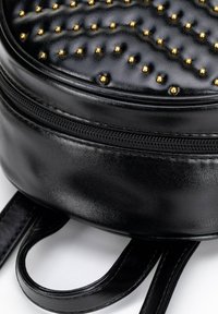 Czarna skórzana plecak o okrągłym kształcie, teksturowanej powierzchni z złotymi ćwiekami oraz zamknięciem na zamek błyskawiczny wzdłuż bocznych i górnych krawędzi.