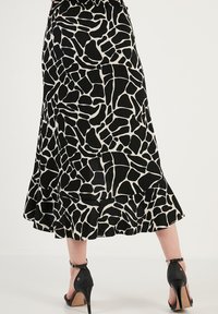 Fustă cu imprimeu de girafă alb-negru, cu margine evazată și detaliu volă. Fabricată dintr-un material texturat, cu talie elastică. Tocuri înalte vizibile.