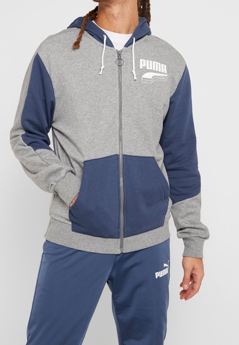 Haut zippé gris et bleu marine avec capuche à cordon, poches avant, poignets côtelés et logo Puma imprimé sur la poitrine.