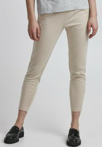 Beige tapse broek gemaakt van zachte stof, met een gladde textuur en gestikte details. Draagt met zwarte loafers voor contrast.