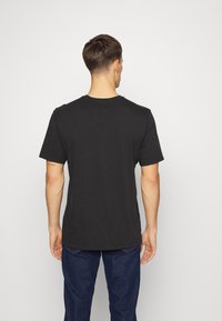 Černé bavlněné tričko s krátkým rukávem a kulatým výstřihem, zobrazené z pohledu zezadu. Hladká textura, volný střih a bez viditelných log.