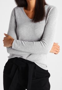 Maglia a maniche lunghe grigio chiaro con scollo a V, texture a coste e silhouette aderente, abbinata a pantaloni neri con cintura annodata.