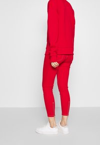 Sudadera roja con leggings ajustados rojos a juego, que presentan costuras blancas y detalles con cremallera en los tobillos, combinados con zapatillas blancas.