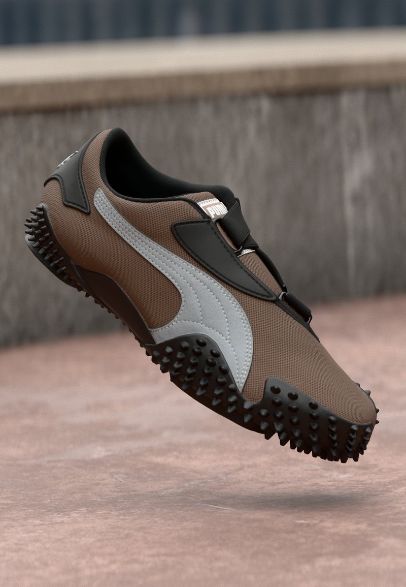 Pruun spordijalats, millel on tekstureeritud ülemine osa, mustad aktsendid ja valge küljeriba. Omab ümarat varbaosa ja harjastega kummist tallat, mis tagab haarde.