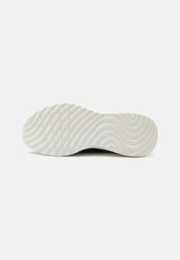 Semelle d'une sneaker avec une texture en caoutchouc blanc ondulée et des rainures horizontales. Le bord est légèrement surélevé et arrondi, avec une surface lisse.