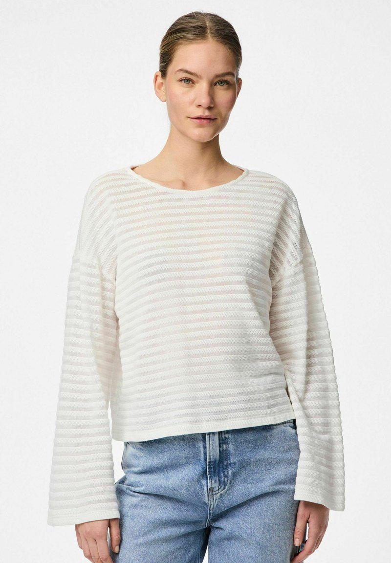 Maglia a maniche lunghe bianca a righe, realizzata in tessuto strutturato, con scollatura rotonda e vestibilità rilassata, abbinata a jeans denim blu chiaro.