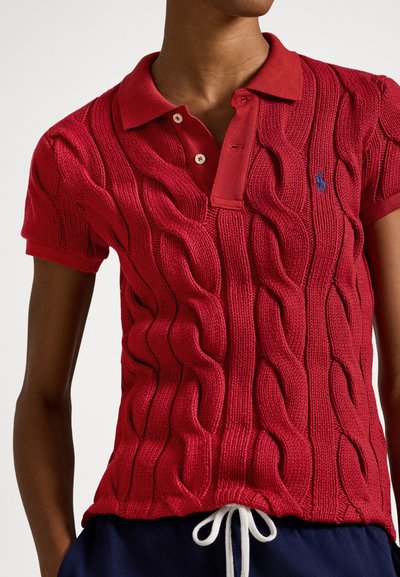 Rdeča pletena polo majica z izrazitim vzorcem v obliki pletenice, kratkimi rokavi in ovratnikom z dvema gumboma. Majhen logotip na prsih.