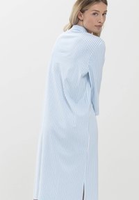 Robe chemise rayée bleu clair et blanche avec col, manches longues, fentes latérales et coupe décontractée. Fabriquée en tissu doux avec des rayures verticales.