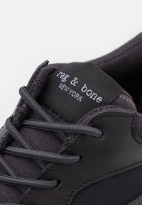Sneaker noir avec une tige en cuir et textile, doté d'une fermeture à lacets plate, d'une étiquette marquée "rag & bone NEW YORK" et d'accents texturés.