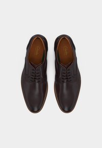 Ζευγάρι ανδρικά παπούτσια δερμάτινα σε σκούρο καφέ χρώμα, με κορδόνια και στρογγυλεμένες μύτες, φαίνονται από πάνω σε λευκό φόντο.
