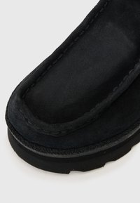 Black suede slip-on shoe featuring a rounded toe, raised stitching along the edges, and a textured rubber sole for grip.