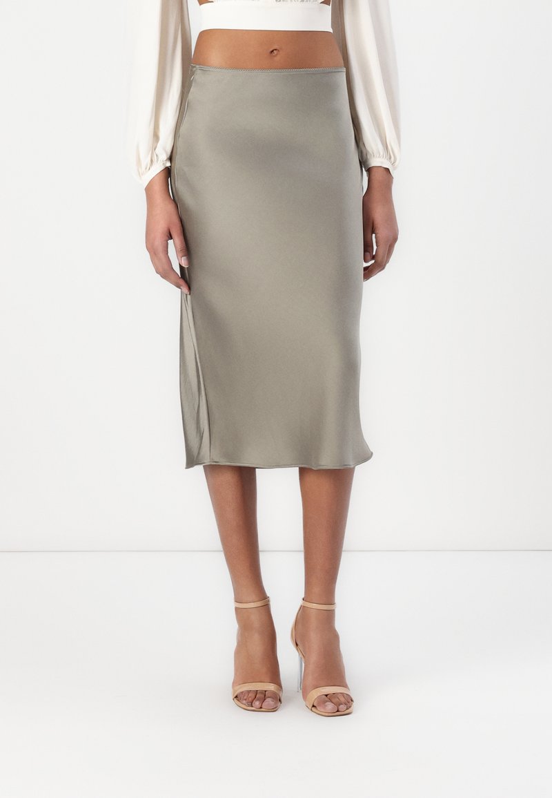 Satin-Midikleid in Olivgrün mit einem Seitenschlitz und glatter Textur. Kombiniert mit nude-farbenen Riemchenschuhen.