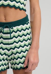 Kudotut shortsit, joissa on vihreä, valkoinen ja tummanvihreä zickzack-kuvio. Varustettu ribbiresorilla, jossa on naru ja aallotettu helma.