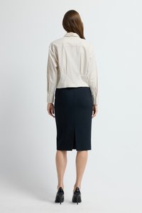 Beige kort skjorta med krage, kombinerad med en marinblå pennkjol med slits bak, bärs med svarta högklackade skor.