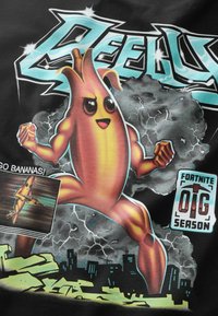 Sort T-shirt med en livlig tegneseriestil bananfigur med muskuløse arme, sat mod en baggrund af lyn og ruiner, mærket "Fortnite."