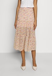 Jupe midi florale dans des couleurs pastel, présentant un design à volants, un tissu doux et une silhouette évasée. Associée à des escarpins beiges à bout pointu.