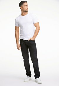 Witte T-shirt met ronde hals gecombineerd met marineblauwe jeans. Model staat in een relaxte pose en draagt witte sneakers. Soepele stof, aansluitend ontwerp.