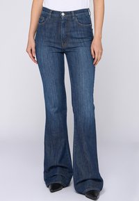 Jeans de mezclilla acampanados en azul oscuro con una textura suave. Presenta cinco bolsillos, botón de metal y costuras contrastantes a lo largo de las costuras.