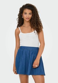 Top in maglia bianca con spalline sottili, abbinato a una gonna A-line in denim blu. La gonna presenta una vita arricciata e una vestibilità casual.