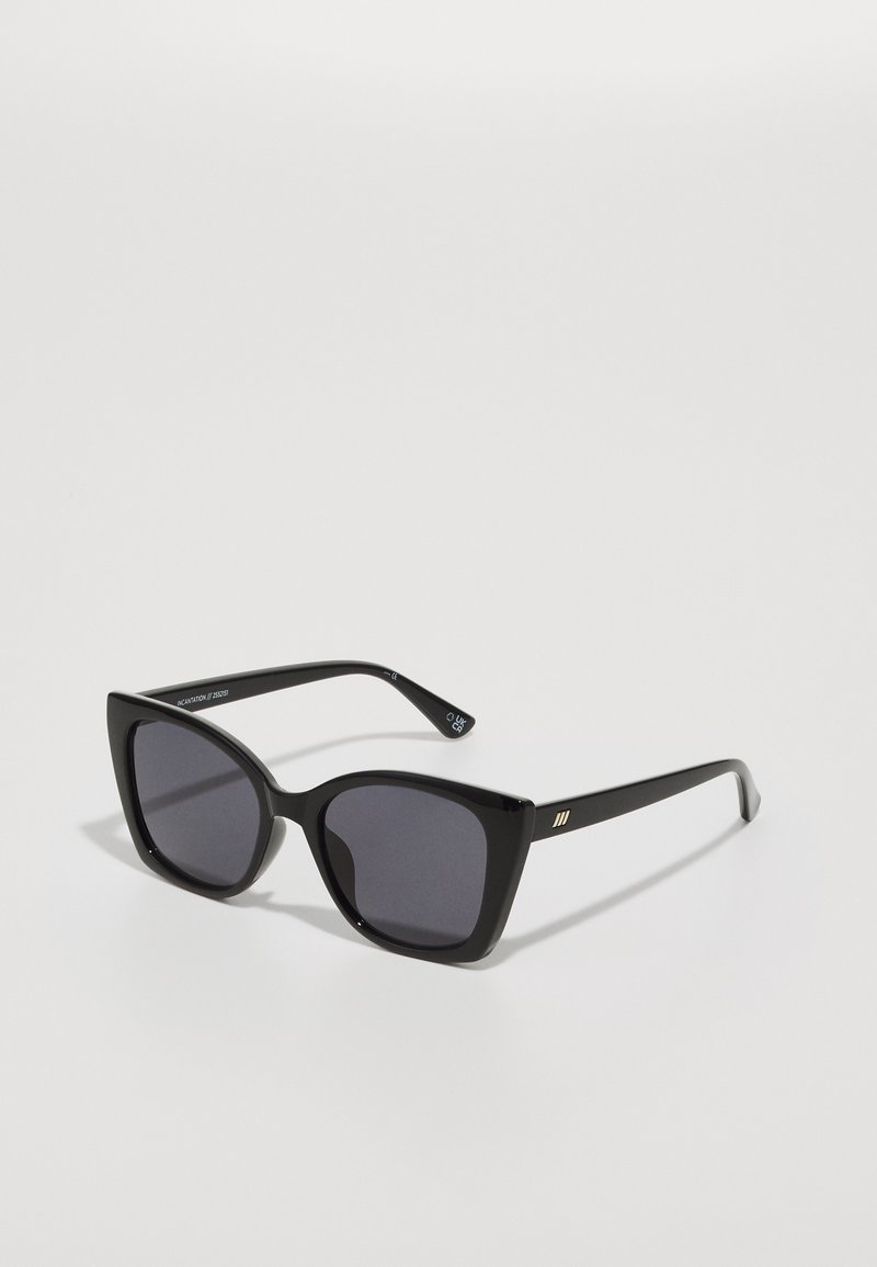 Óculos de sol pretos de plástico com uma armação larga, design de olhos de gato, lentes escuras e um detalhe dourado nas hastes. Textura suave, acabamento brilhante.