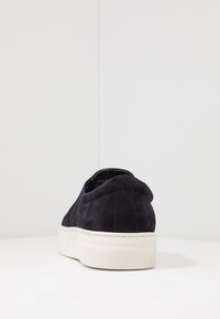 Sapato slip-on de camurça azul-marinho com sola de borracha branca. Apresenta bico arredondado e detalhes costurados no calcanhar. Design minimalista.