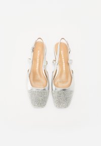 Sudraba slingback soļi ar gludu metālisku virsmu un acs rotājumu no mazām rhinestone akmeņiem pie pirksta, ar mīkstu ieliktni.