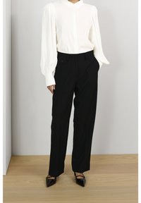 Witte, gestructureerde blouse met pofmouwen, gecombineerd met hoge zwarte broeken en puntige zwarte schoenen. Schone, minimalistische uitstraling.