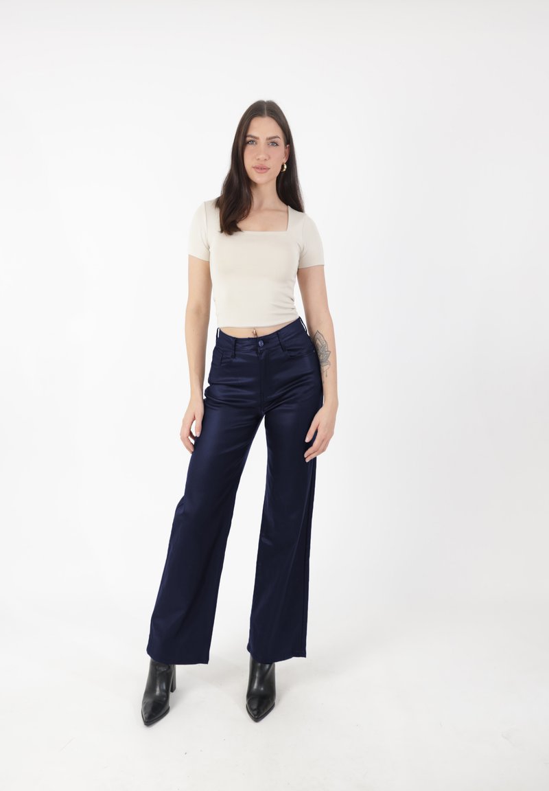 Beżowa dopasowana bluzka z krótkim rękawem, zestawiona z granatowymi satynowymi spodniami typu wide-leg oraz czarnymi zaostrzonymi botkami o kostkę. Prosty design i neutralne kolory.