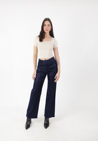 Top beige aderente con maniche corte, abbinato a pantaloni ampi in satin blu notte e stivaletti neri con punta. Design semplice e colori neutri.