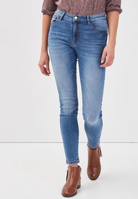 Jeans de mezclilla azul de cintura alta con un corte ajustado, que cuentan con dos bolsillos frontales, costuras en contraste y un diseño elegante hasta el tobillo.