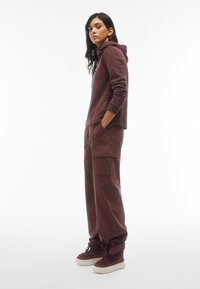 Felpa color mogano con tasca a canguro e polsini aderenti, abbinata a pantaloni cargo larghi color mogano con tasche laterali e vestibilità rilassata.