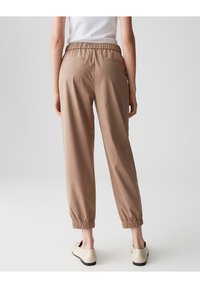 Lockere, knöchellange Hosen aus hellbraunem Baumwollmix. Mit elastischem Bund und Seitentaschen sowie elastischen Bündchen am Saum.