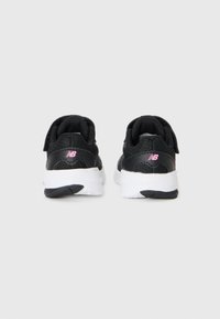 Paire de baskets New Balance noires avec semelles blanches, vues de l'arrière sur un fond blanc uni.
