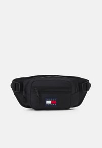 Fanny pack en tissu noir avec un compartiment zippé à l'avant, une sangle ajustable et un patch logo rectangulaire aux couleurs rouge, blanc et bleu.