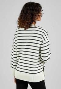 Gestreifter Pullover in Creme mit schwarzen Streifen; verfügt über einen lockeren Schnitt, einen gerippten Saum und seitliche Schlitze für zusätzlichen Komfort und Detail.
