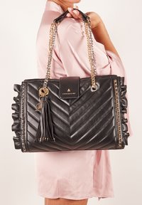 Borsa a tracolla in pelle nera con trapuntatura a zigzag, manici in catena oro e argento, dettagli a volant ai lati e una tassel decorativa.