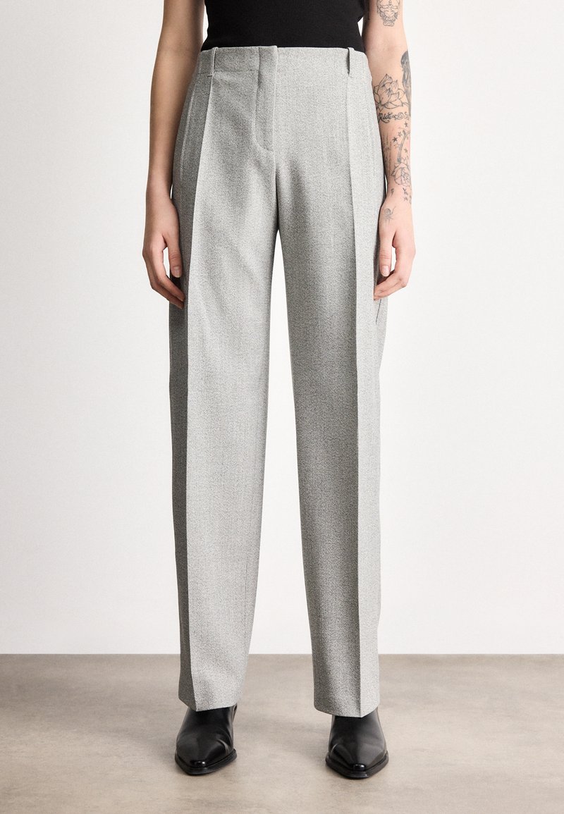 Hallid kõrge vöökohaga püksid tekstuurse viimistlusega, esikäevaitsed, küljetaskud ja lõdva istuvusega, kombineeritud mustade pahkluu saapadega.