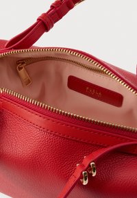 Rød læderhåndtaske med struktureret overflade, guldtonet lynlås og en glat inderside med et mærkelabel. Justerbar rem inkluderet.