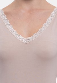 Beige V-neck top with a delicate, floral lace trim around the neckline; smooth, slightly textured fabric.