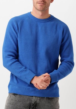 Blauer Langarm-Pullover mit Rundhalsausschnitt und gerippter Textur, in einfarbigem Design und mit Standardbündchen. Getragen über einer hellen Jeans.