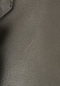 Gros plan d'un matériau en cuir texturé gris foncé avec un bord visible et un trou de couture dans le coin supérieur gauche.