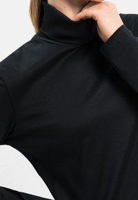 Schwarzes Rollkragoberteil aus einem weichen, dehnbaren Stoff. Mit hohem Kragen und langen Ärmeln, glatt in der Textur und tailliert geschnitten.