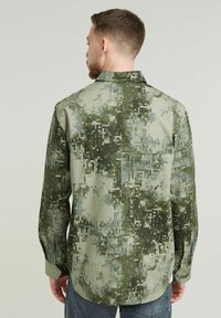 Långärmad skjorta i pixelmönstrad grön och grå kamouflage, med en klassisk krage och knappade manschetter, tillverkad av ett mjukt tyg.