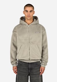 Pelēks džemperis ar rāvējslēdzēju, izgatavots no m�īksta, strukturēta auduma. Tam ir priekšējā kabata un ribota aproce, uz krūtīm redzama logotipa uzlīme.