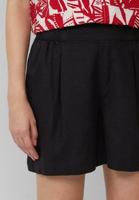 Shorts neri in lino con fronte plissettato, cintura elastica e tasche laterali. Il tessuto ha una texture liscia e una vestibilità comoda.