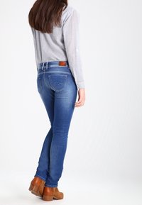 Smala jeans i mörkblå denim med en blekt finish, med designade bakfickor och en brun läderpatch i midjan. Bruna klackskor.