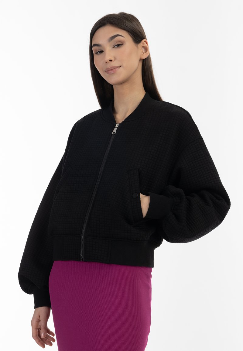 Zwarte bomberjack van textuurstof, met ritssluiting en oversized mouwen. Bevat zijzakken en geribbelde manchetten; casual en comfortabele uitstraling.