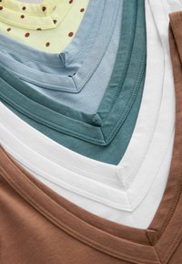 T-shirts en coton à col en V empilés dans les couleurs marron, blanc, sarcelle, bleu et jaune avec des pois marron, présentés en gros plan.